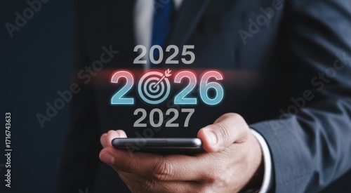 Wallpaper Mural Business vision, target of years : A person holding a smartphone, showcasing the years 2025, 2026, and 2027 overlaid with a striking bullseye, symbolizing future business targets and goals. Torontodigital.ca