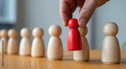 Selection of the Outstanding : A focused perspective showcases a hand carefully selecting a vibrant red wooden figure from a line of identical pieces.
