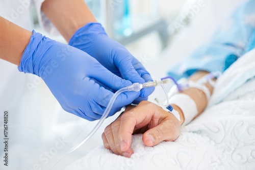 Close-up of a nurse's hands in blue gloves adjusting an intravenous therapy IV drip for a patient in a hospital bed
