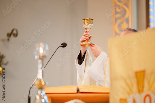 Catholic priest celebrating Holy Mass during liturgy with chalice, Bible, and liturgical vestments inside church, Eucharist and communion ceremony in Christian tradition