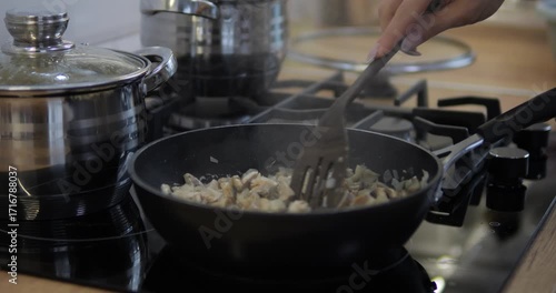 The hostess is preparing a dish with mushrooms and pasta in the kitchen. A stove with a frying pan and pots.