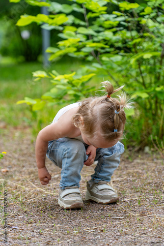 Curious toddler with playful pigtails intently exploring natural ground in vibrant green outdoor environment