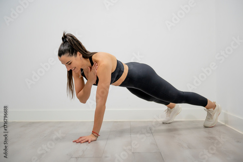 Woman holding plank position with one hand touching shoulder for core stability strength training