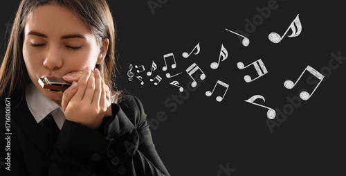 Young woman playing harmonica on dark background