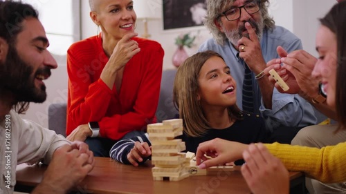 Excited multi-generational family gathering playing Jenga at home. Caucasian people together Digital detox domestic with board games. A woman is taking a block of wood out of the tower and it falls