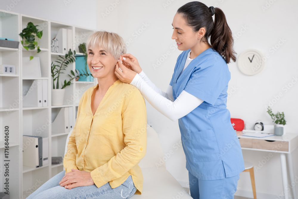 Fototapeta premium Doctor putting hearing aid on mature woman's ear in clinic