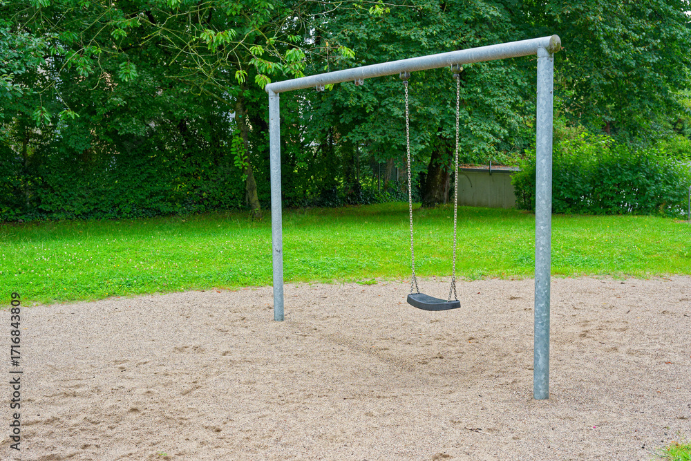 Fototapeta premium Playground swing frame with one black seat and green lawn