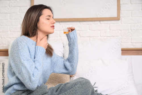 Ill young woman taking cough syrup in bedroom