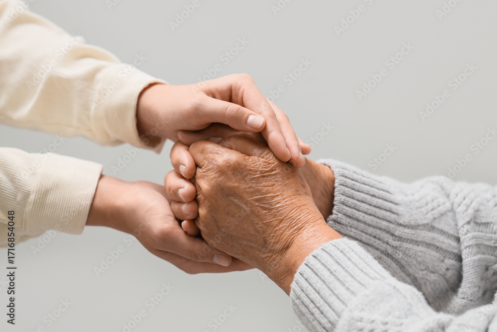 Fototapeta premium Woman holding grandmother's hands on light background