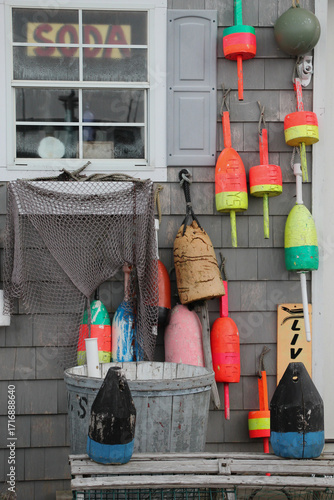 colorful buoys and netting used for lobster traps on side of gray weathered lobster shack 