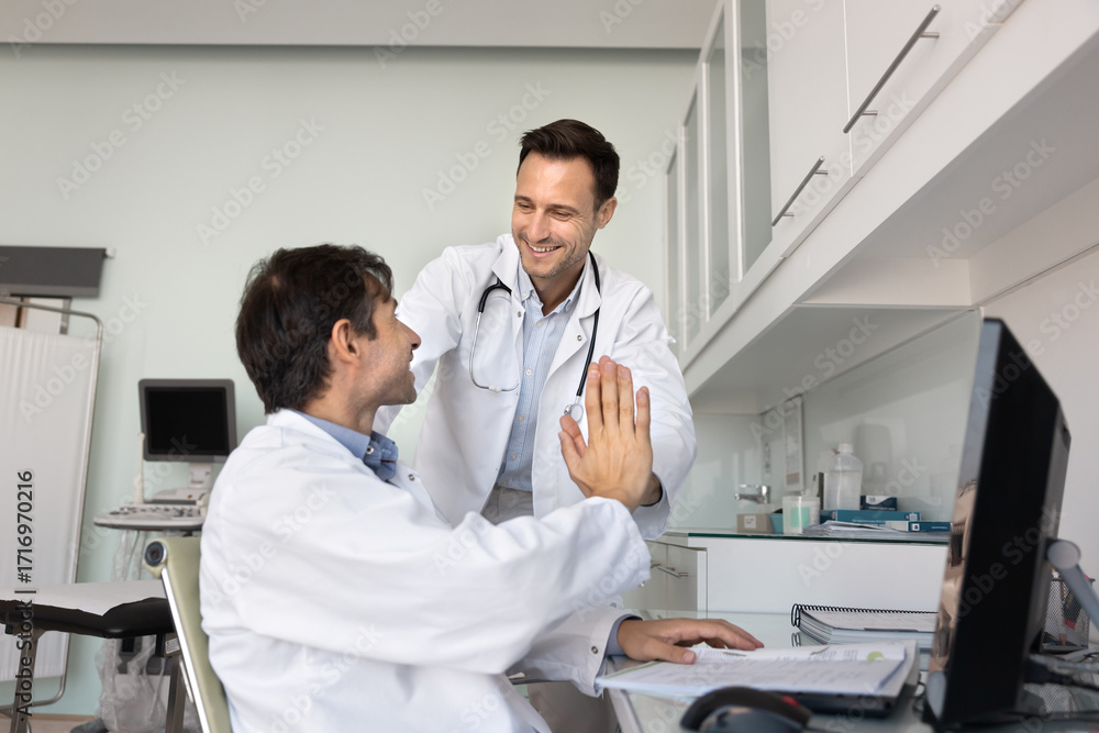 Fototapeta premium Two happy excited male doctors exchange high five at workplace