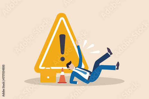 Businessman falls down near a large yellow warning sign and orange traffic cone