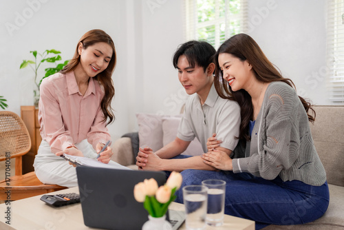 Experienced Asian financial advisor guides young couple home discussing comprehensive health insurance plans property investment future wealth building