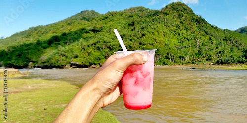 Fresh Watermelon Juice Drink Held by Hand Facing the Beautiful Tropical Mountain Landscape Background with Refreshing Natural Scenery