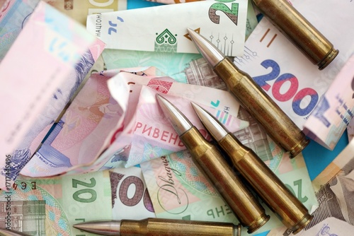 Many rifle bullets lies on lots of ukrainian money bills close up