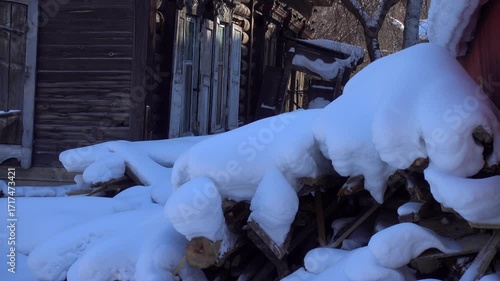 Atmospheric winter abandoned courtyard among old wooden log houses. Authentic Slavic rural izba with poverty details, trash scattered in snow. Evokes decaying past, melancholic mood of forgotten place