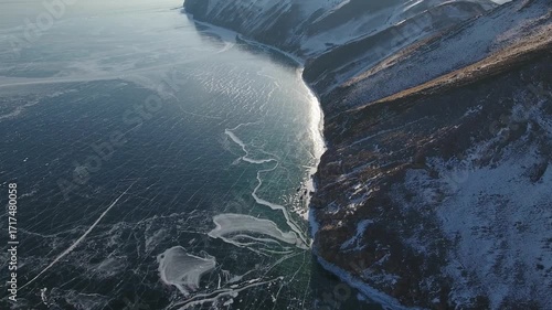 Epic helicopter shot over frozen Lake Baikal in winter. Vast cracked ice patterns, rocky coastline, snow-capped mountains of Siberia and Buryatia Stunning UNESCO world heritage landscape unique nature