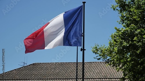 Flag with the colors red, white, and blue. It is flying in the air. The flag is on a pole
