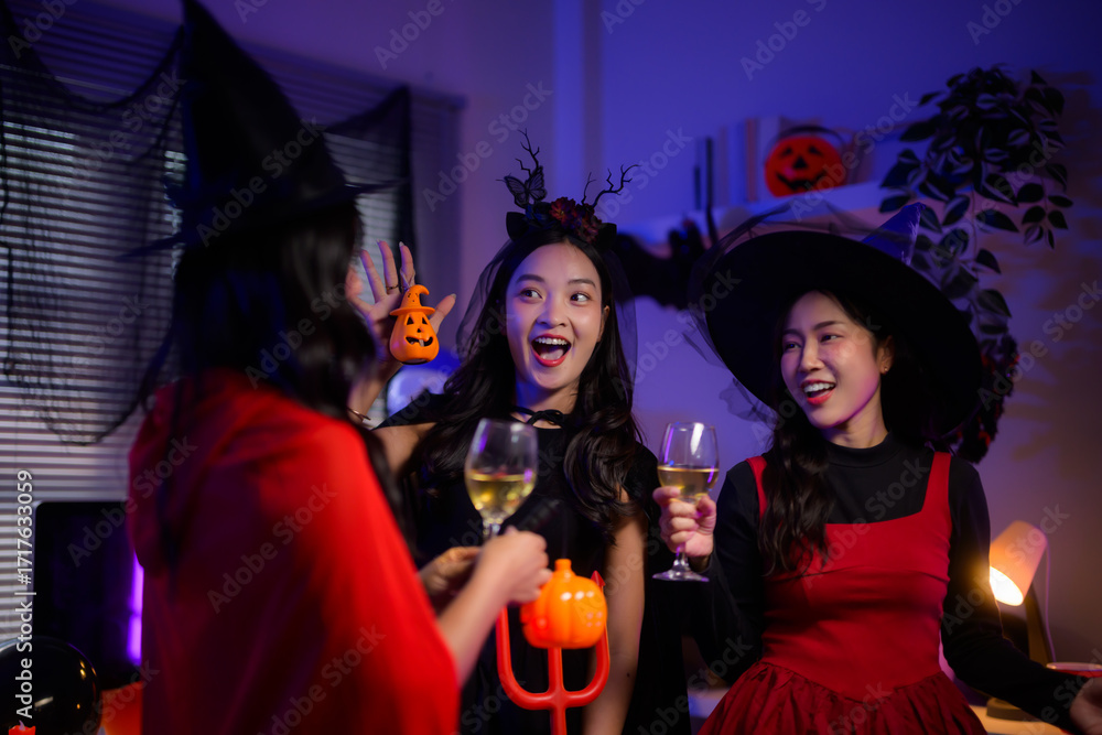 Fototapeta premium Excited young Asian women celebrating Halloween party, laughing and toasting drinks in spooky costumes