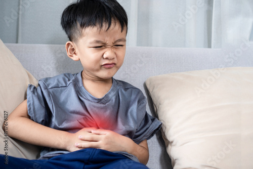 Asian boy suffering from stomachache due to food poisoning, feeling sick with diarrhea and nausea, showing symptom of digestive illness