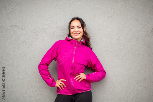 Happy woman posing in pink windbreaker against gray wall