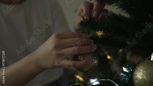 Woman's hands decorating a christmas tree with golden baubles