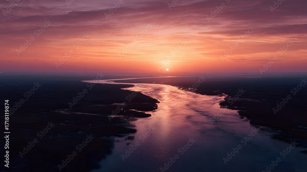 Fototapeta premium Aerial view of a wide river delta at sunset with winding channels and an orange glow