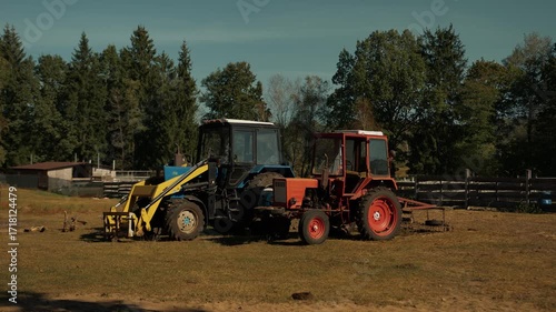 Two tractors parked in clearing next to cattle pen with wooden fence