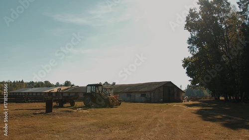 New tractor for farm work and stacks of roofing slates on lawn near huge cattle paddock on ranch.