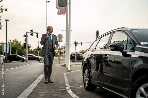 Wallpaper Mural Senior businessman walking on sidewalk and talking on phone near car Torontodigital.ca