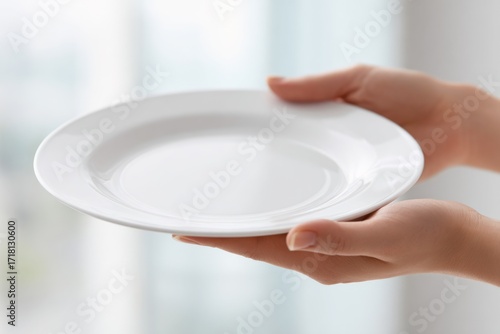 Clean, empty and white plate held by hands, blurry background