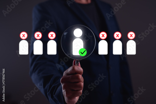 A person holding a magnifying glass focuses on an individual among a group, symbolizing selection or evaluation in a professional context.