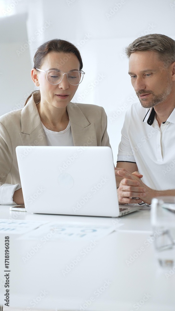 Obraz premium Businessman and adult businesswoman reviewing marketing analytics on laptops, working together strategically in contemporary office workplace. Business people concept