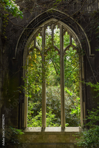 Bild auf Leinwand Abandoned St Dunstan in the East Church, featuring a gothic window surrounded by overgrown plants, showcasing a blend of architecture and nature