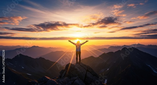 Person stands on mountain peak arms raised at sunrise inspirational achievement concept