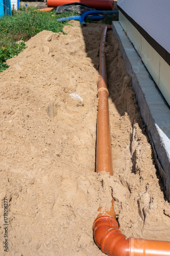 Underground drainage pipe installation next to house foundation with sand backfill at residential construction site.