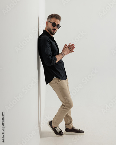 confident cool man with sunglasses rubbing palms and leaning on a wall