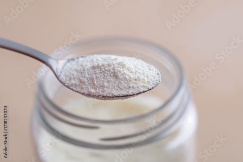 Spoon with creatine monohydrate powder close up over glass jar