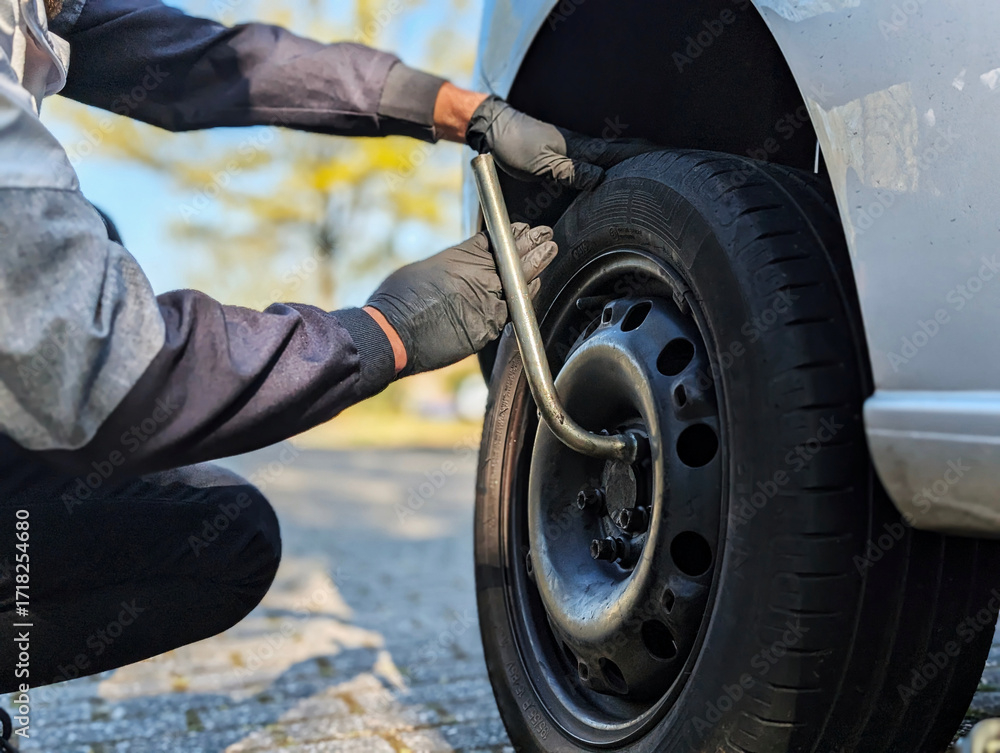 Fototapeta premium A man fastening or loosening wheel nuts during seasonal tire replacement. Symbol of car repair, safety check and mobility.