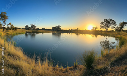Serene sunset over tranquil pond reflecting golden hues, surrounded by lush grass and trees in peaceful rural landscape, flat lay composition