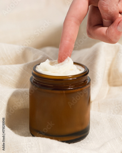 Woman's finger reaching for whipped beef tallow moisturizer in amber glass jar