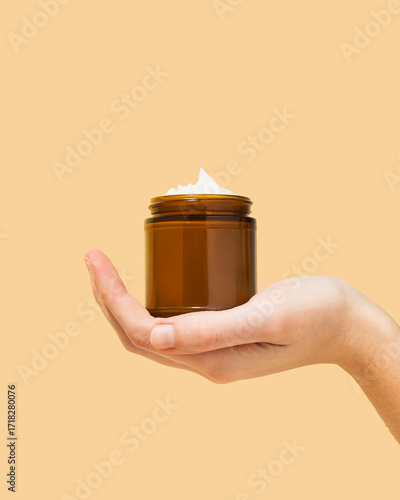 Woman holding amber glass jar of beef tallow moisturizer on pastel yellow background 