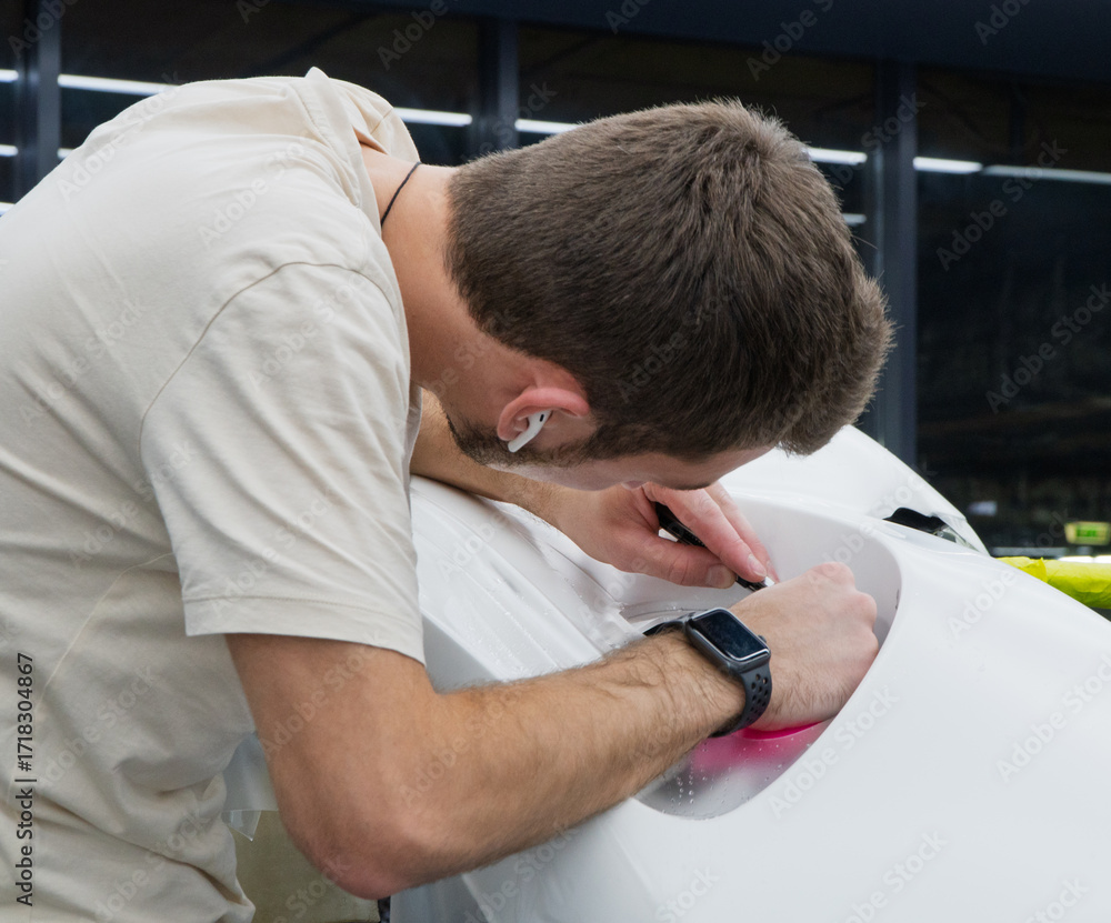 Fototapeta premium A car wrapping specialist applies a polyurethane film to the car. Detailer smoothes PPF. Car wrapping, detailing, tuning and styling. PPF protective film against chips and scratches. Selective focus.