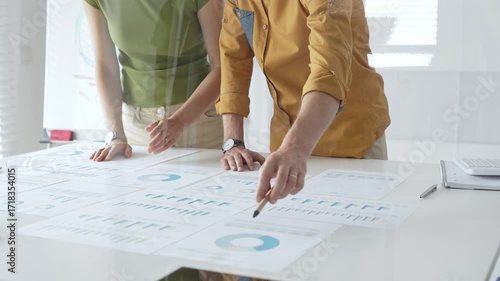 Business professionals analyzing financial reports, pointing at charts during collaborative meeting, discussing data with focused professional demeanor