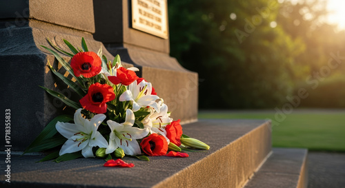 Remembrance Day flowers grace somber monument in gentle sunlight. Remembrance Day poppies and lilies laid at base of memorial honors those who served,