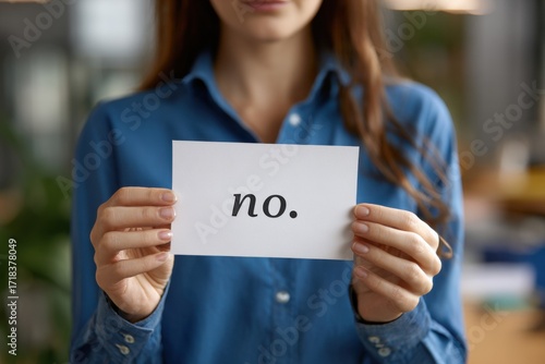 A woman confidently holds up a card displaying the word 'no', symbolizing assertiveness and the importance of setting boundaries in personal and professional life.