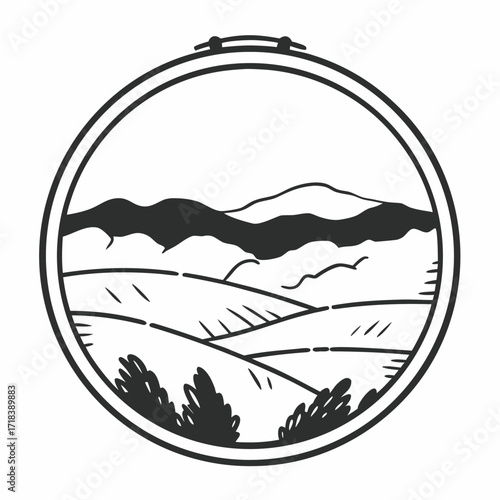 Circular embroidery hoop framing a stylized black and white landscape with rolling hills distant mountains and scattered trees evoking a sense of rustic charm and handcrafted artistry