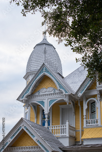 The exterior of a vintage Victorian heritage home with pale yellow wooden clapboard siding. There's a white decorative turret on the roof. The trim on the two-story estate is white.