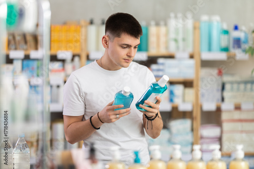 Foto Guy chooses a mouthwash in a pharmacy against the background of racks with medic