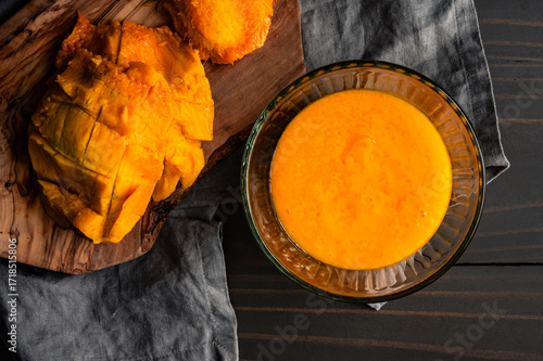 Homemade Mango Puree in a Glass Bowl: Pureed tropical fruit with mango peel and seed on a wooden cutting board